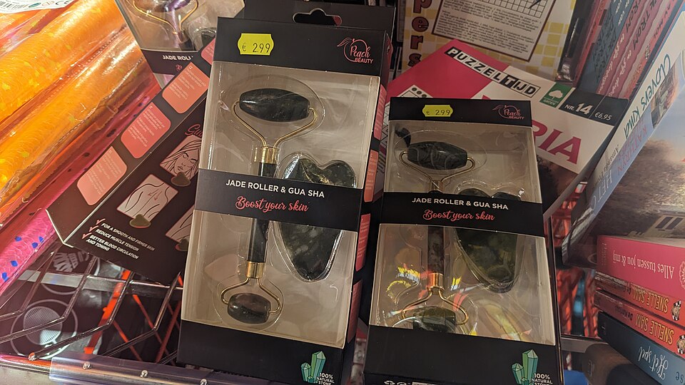 A jade roller and gua sha stone laid side by side on a shelf