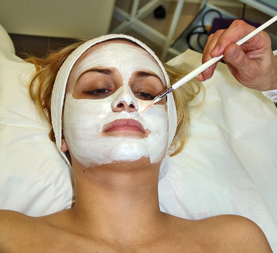 A woman with a cosmetic face mask spread evenly over her face