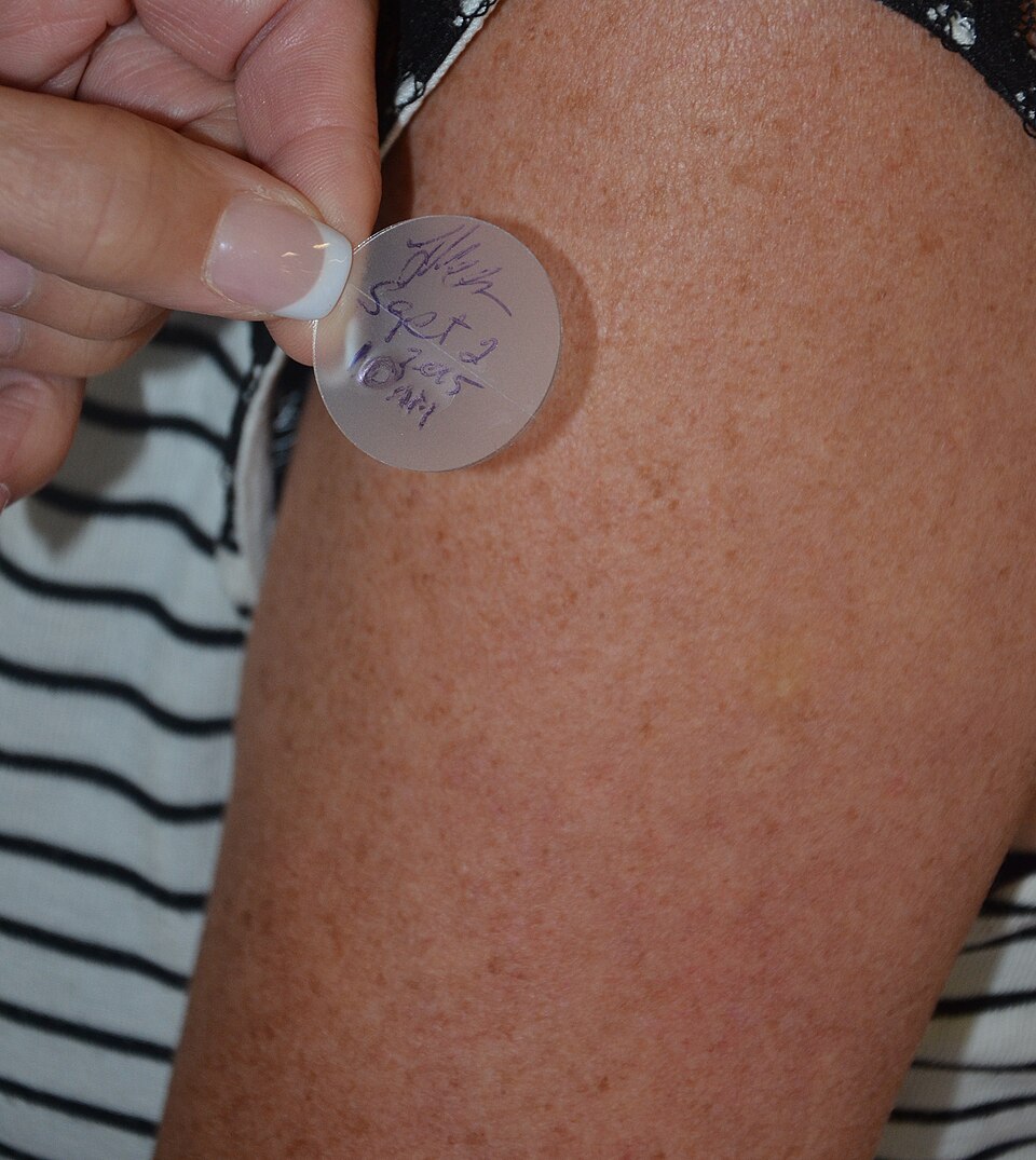A patch being pressed onto the skin of an upper arm by hand