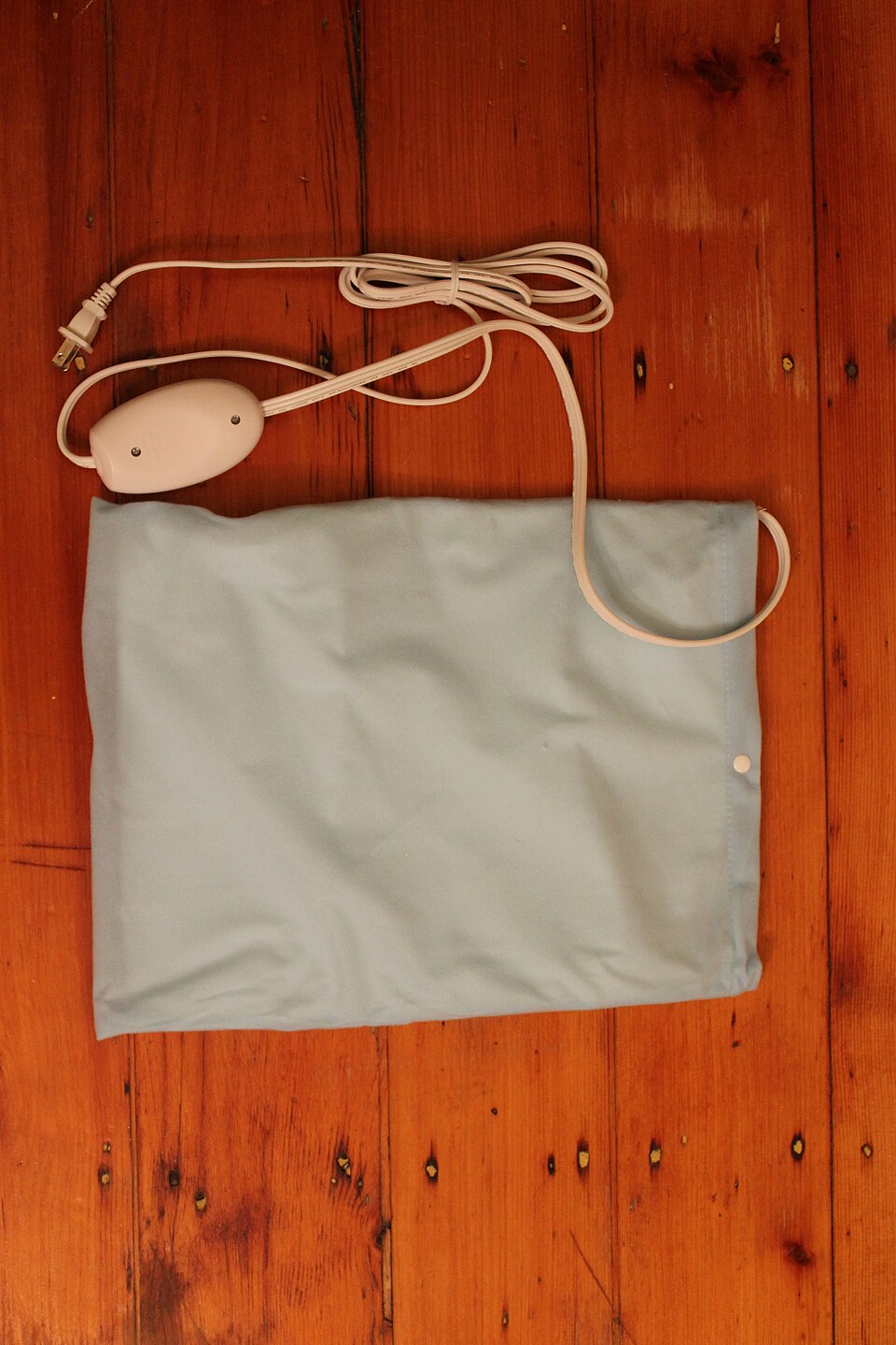 A rectangular heating pad with its fabric cover and cable